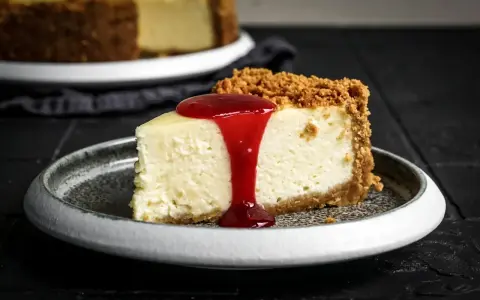 Ein Stück cremiger American Cheesecake mit Keksboden und roter Fruchtsauce. Perfekt für Ihr American Cheesecake Rezept!