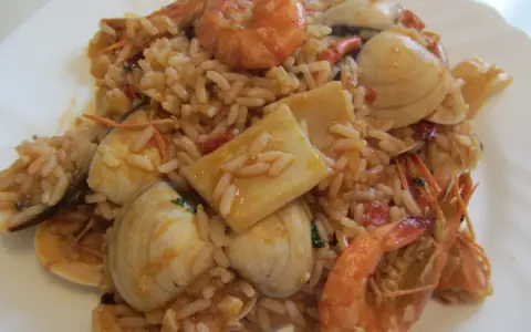 Ein köstlicher arroz de marisco mit Garnelen, Muscheln und Tintenfischstücken, serviert auf einem weißen Teller.