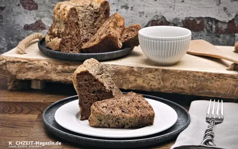 Zwei Stücke eines rustikalen, dunklen Diabetiker Kuchens auf einem Teller, daneben eine Schüssel und ein Messer.