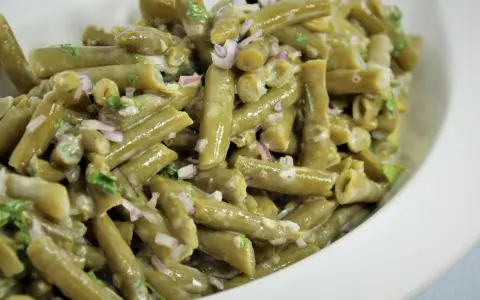 Grüner Bohnensalat mit cremigem Dressing, roten Zwiebeln und Kräutern in einer weißen Schüssel.