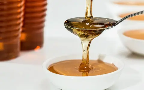 Goldener Sirup fließt von einem Löffel in eine Schüssel. Ob es sich um Agavendicksaft oder Honig handelt, ist schwer zu sagen.