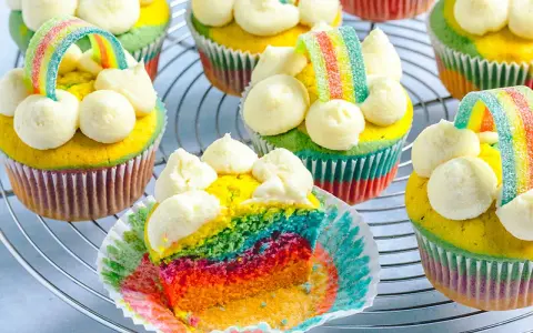 Bunte regenbogen muffins mit weißem Frosting und Gummibärchen-Regenbogen-Deko auf einem Gitter.