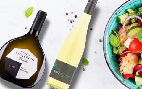 Zwei Flaschen Wein, eine davon eine Scheurebe mit fruchtigem Geschmack, neben einem frischen Salat.