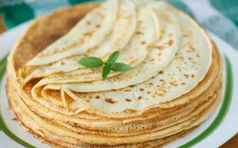 Ein Stapel goldbrauner Pfannkuchen, wie nach Omas Pfannkuchen Rezept, mit einem Minzblatt garniert.
