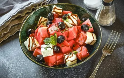 Erfrischender Melone Feta Salat mit schwarzen Oliven und Minze, beträufelt mit Balsamico-Glasur.