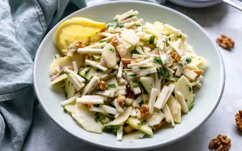 Frischer sellerie salat mit Äpfeln, Walnüssen und Kräutern, garniert mit einer Zitronenspalte.