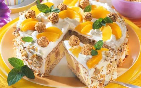 Eine köstliche Giotto Torte mit Pfirsichspalten, Sahne und gehackten Mandeln. Kleine Pralinen und Minzblätter zieren die Torte.
