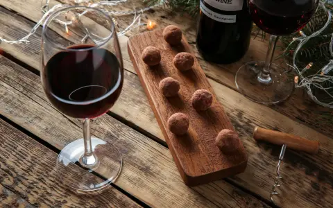 Ein Glas Rotwein und Schokolade-Trüffel auf einem Holzbrett, daneben eine Flasche Rotwein und Lichterketten.