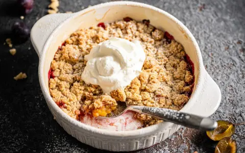 Ein warmer Zwetschgen Crumble mit Haferflocken, gekrönt von einem Klecks Sahne. Ein Löffel hebt die süße Frucht hervor.