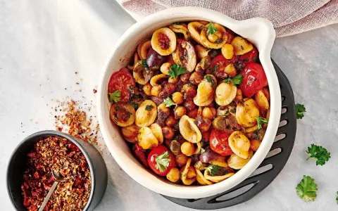 Ein bunter Nudelsalat mal anders: Orecchiette mit Kichererbsen, Kirschtomaten, Oliven und Kräutern in einer Auflaufform. Daneben eine Schale mit Gewürzmischung.