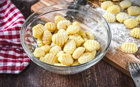 Frisch gemachte Gnocchi in einer Schüssel, bereit zum Kochen. Auf dem Holzbrett liegen weitere Gnocchi, die zeigen, wie einfach es ist, Gnocchi selber machen.