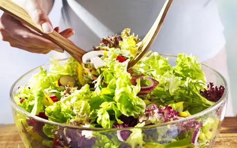 Frischer gemischter Salat mit knackigem Salat, Radieschen, Zwiebeln und Pilzen wird mit Holzsalatbesteck vermischt.