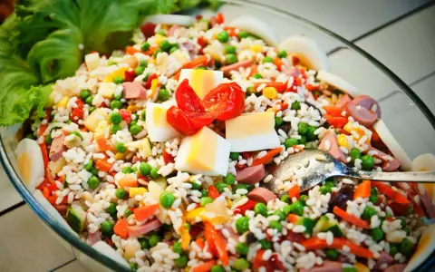 Reissalat mit Erbsen, Karotten, Ei und Wurst – ein gesunder Salat zum Grillen, garniert mit Tomaten und Salatblättern.