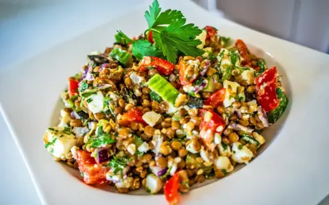 Frischer Linsensalat mit Feta, Paprika, Gurke und Kräutern, garniert mit Petersilie.