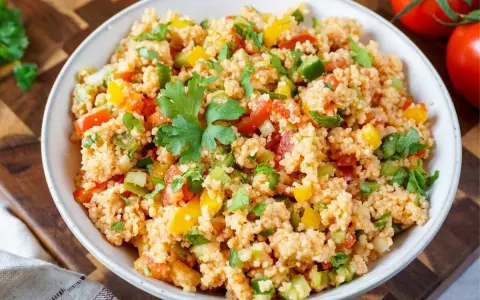 Bunter Couscous-Salat mit Tomaten, Paprika und Petersilie, garniert mit einem Petersilienblatt.