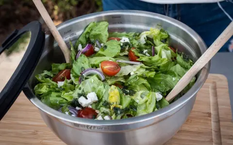 Frischer Salat zum Grillen, zubereitet von Landfrauen. Knackiger Salat mit Tomaten, Zwiebeln und Feta in einer Edelstahlschüssel.