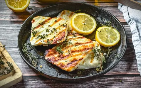 Perfekt gegrillter Halloumi mit Kräutern und Zitronenspalten auf einer Gusseisenplatte. Ein Genuss für alle Sinne!