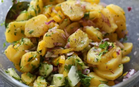Omas sonntagsessen: Kartoffelsalat mit Gurken, Zwiebeln und frischen Kräutern, perfekt gewürzt.