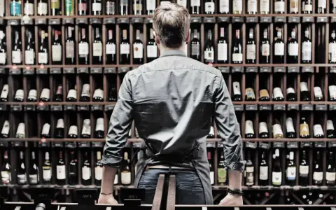 Mann vor Weinregalen, die eine bordeaux jahrgangstabelle studiert.
