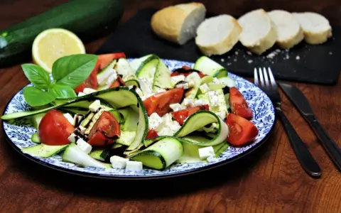 Ein erfrischender, sommerlicher Zucchini-Salat mit Tomaten und Feta, garniert mit Basilikum und Balsamico. Dazu Baguettescheiben.