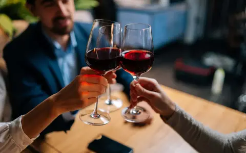 Drei Personen stoßen mit Rotwein an. Sie halten das weinglas richtig, am Stiel, um die Temperatur des Weins zu bewahren.