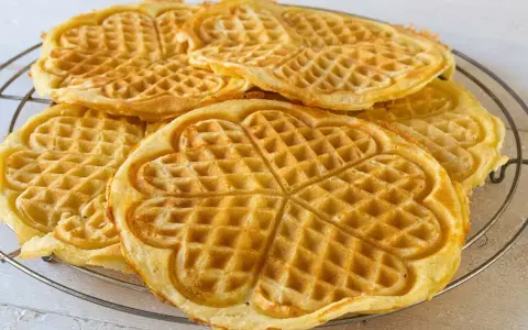 Goldbraune Herz-Waffeln, frisch gebacken aus waffelteig ohne butter, liegen auf einem Gitter.