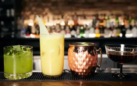 Vier kunstvoll zubereitete Cocktails, die die Definition eines perfekten Drinks verkörpern: ein grüner, ein gelber, ein Moscow Mule und ein dunkler Aperitif.