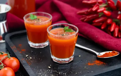 Zwei Gläser würziger mexikanischer Tomatensaft, garniert mit Petersilie, neben frischen Tomaten und Chilis.