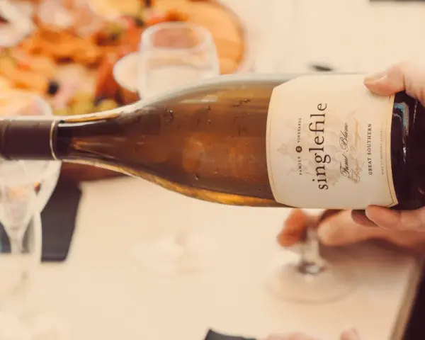 Eine Hand gießt einen **fumé wein** aus einer Flasche in ein Glas. Im Hintergrund ist eine Platte mit Speisen zu sehen.