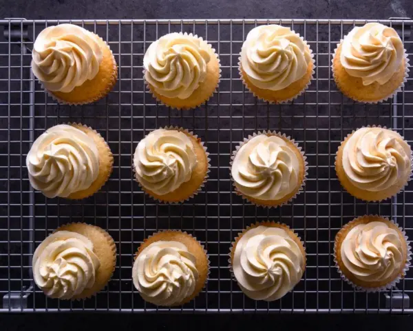 Zwölf Cupcakes mit cremiger deutscher Buttercreme auf einem Gitter.