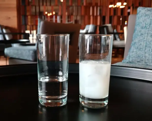 Zwei Gläser auf einem Tisch: eines mit klarem Wasser, das andere mit milchigem Ouzo. Ein Vergleich zwischen Raki und Ouzo.