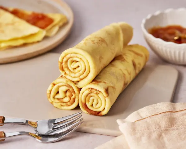 Gestapelte Quark Pfannkuchen, goldbraun gebacken, mit einer Schale Marmelade und Gabeln daneben.