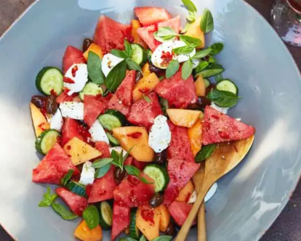 Erfrischender Melonensalat mit Mozzarella, Gurke und Basilikum auf einem grauen Teller.