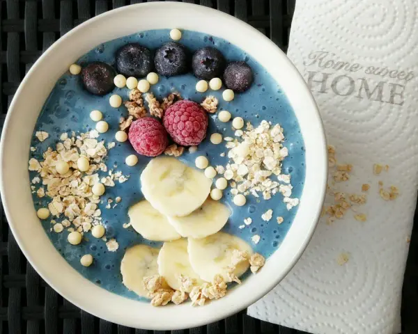 Blauer Smoothie-Bowl mit Blaubeeren, Himbeeren, Bananenscheiben und Granola. Perfekt für gesunde smoothie rezepte.