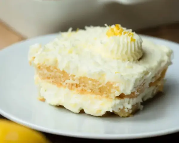 Ein Stück cremiges Limoncello Tiramisu, garniert mit Zitronenzesten und einem Tupfer Sahne, auf einem weißen Teller.