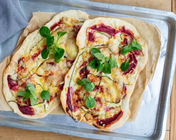 Zwei Flammkuchen mit Zucchini und Roter Bete, garniert mit frischen Blättern. Eine histaminarme Alternative, bei der man auf Weintrauben verzichtet.