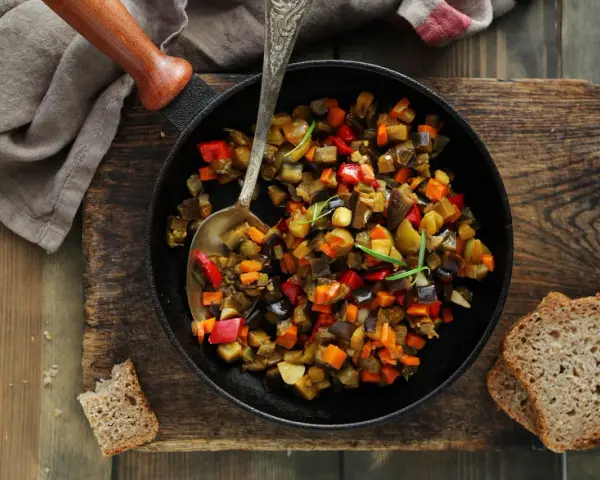 Ratatouille rezept: Buntes Gemüse aus Aubergine, Paprika und Karotten in einer Pfanne, serviert mit Brot.