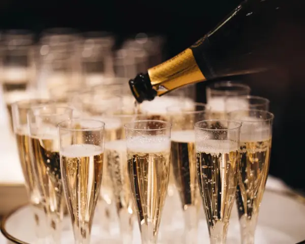 Sekt wird in Gläser gefüllt, die auf einem Tablett stehen. Die Bläschen steigen auf und erinnern daran, woher Champagner kommt.