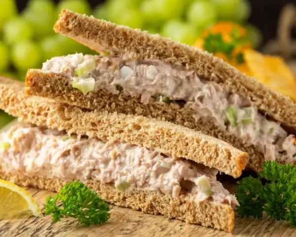 Zwei Tramezzini mit Thunfischsalat, Sellerie und Zwiebeln auf Vollkorntoast. Dazu Trauben, Zitrone und Petersilie. Perfekt für schnelle Tramezzini Rezepte.