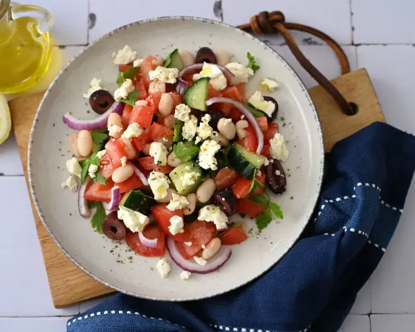 Frischer griechischer Bohnensalat mit Tomaten, Gurken, roten Zwiebeln, Oliven und Feta. Ein Spritzer Olivenöl und Zitrone machen ihn perfekt.