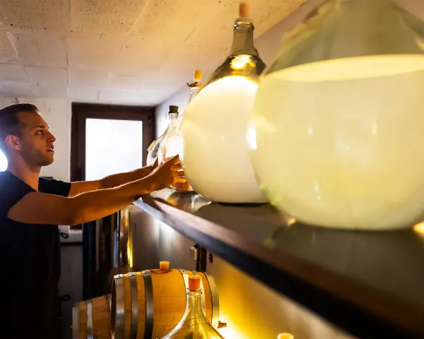 Mann sortiert Flaschen für die Gin-Lagerung. Daneben stehen Fässer und große Glasballons.