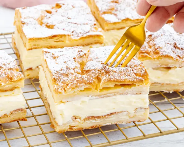 Ein goldener Löffel sticht in ein Stück polnischer Puddingkuchen, bestäubt mit Puderzucker.