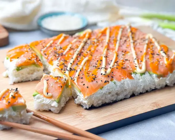 Rechteckiges Sushi mit Lachs und Avocado, verziert mit Mayonnaise und Sesam. Perfekt, um Sushi selber machen zu lernen!