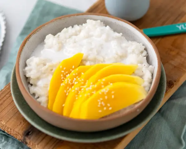 Schüssel mit cremigem **sticky rice** und saftigen Mangoscheiben, bestreut mit Sesam. Ein köstlicher Genuss!