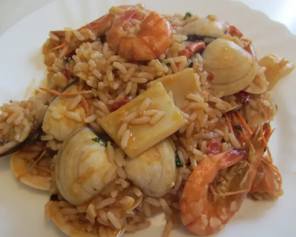Ein köstlicher arroz de marisco mit Garnelen, Muscheln und Tintenfischstücken, serviert auf einem weißen Teller.
