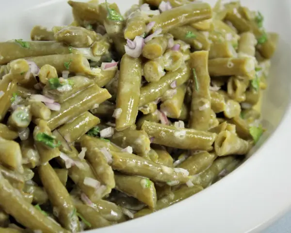 Grüner Bohnensalat mit cremigem Dressing, roten Zwiebeln und Kräutern in einer weißen Schüssel.
