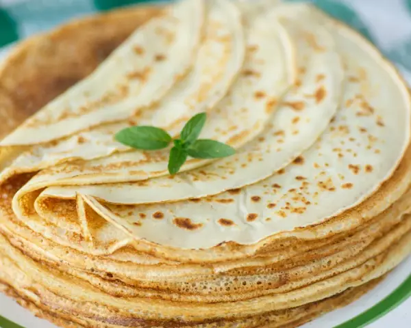 Ein Stapel goldbrauner Pfannkuchen, wie nach Omas Pfannkuchen Rezept, mit einem Minzblatt garniert.