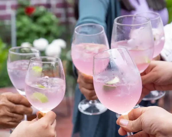 Hände stoßen mit rosafarbenen Sarto Spritz-Cocktails mit Limette und Eis an.