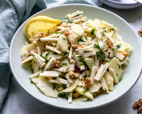 Frischer sellerie salat mit Äpfeln, Walnüssen und Kräutern, garniert mit einer Zitronenspalte.