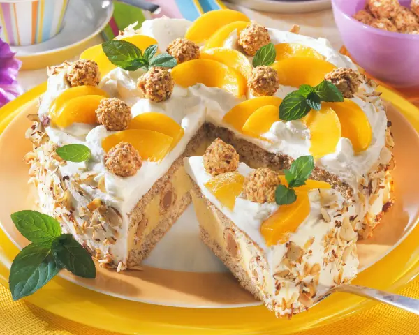 Eine köstliche Giotto Torte mit Pfirsichspalten, Sahne und gehackten Mandeln. Kleine Pralinen und Minzblätter zieren die Torte.